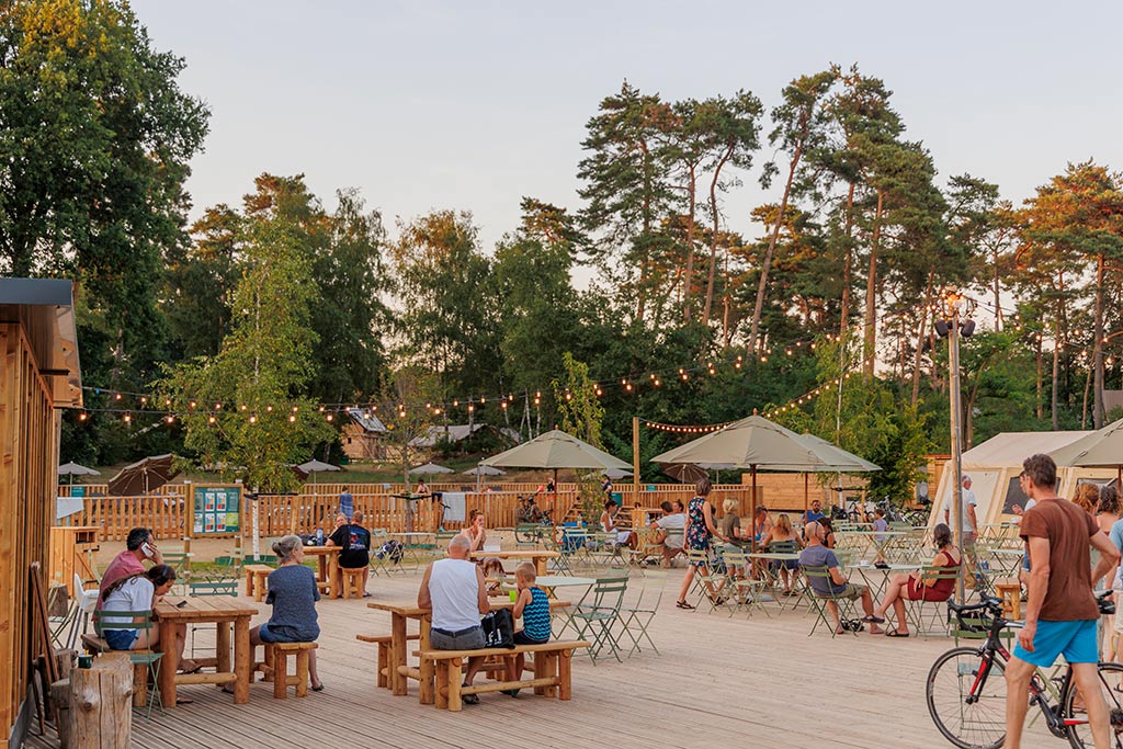 Große Aussenterrasse mit Sitzgruppen, Sonnenschirmen und Gästegruppen umrandet von hohen Bäumen