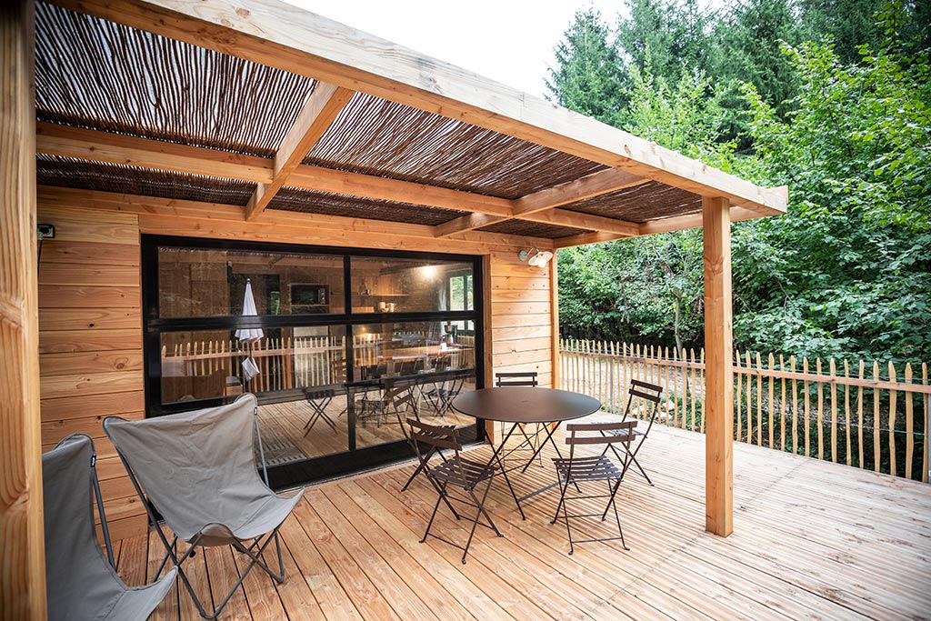 Großes Holz-Chalet mit hölzerner Terrasse und einigen Stühlen rund um einen runden Tisch