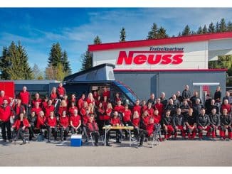 Teambild des Camping-Kaufhauses: rund 60 Personen mit roten oder grauen Pullovern vor Firmengelände bei Freizeitpartner Neuss