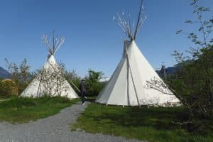 Blauer Himmel im Hintergrund, zwei weiße, große Tipies auf grüner Wiese und Kiesweg dazwischen. 