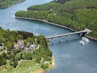 Insel verbunden durch Brücke zum Festland, dazwischen fließt ein blauer Fluss auf dem Boote schwimmen.