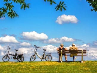 Ein älteres Paar auf einer Parkbank auf einer Wiese, neben ihnen stehen zwei Klapp-E-Bikes