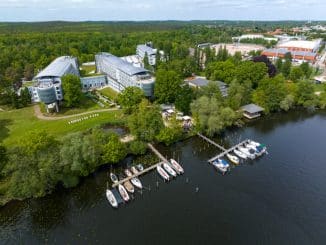 9. Norddeutscher Campingtag 2024: Kongresshotel Potsdam am Templiner See umgeben von grünen Bäumen und Wiesen. Mit Bootsanlegern auf dem See.