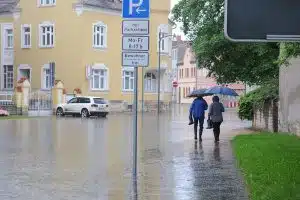 Zwei Personen spazieren unter einem Regenschirm im Hochwasser durch eine Stadt.