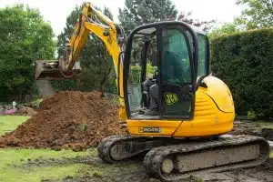 Gelber Bagger mit Schaufel in einem Garten der Erde für den Einbau einer Wasserzisterne aushebt.