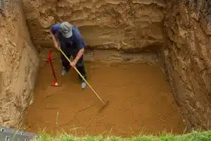 Mann kehrt in einer Erdgrube die für eine Wasserzisterne ausgehoben wurde.