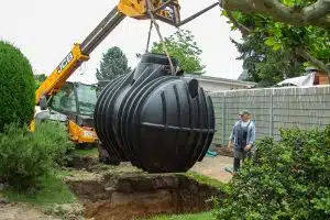 Bagger hebt eine schwarze Wasserzisterne in eine Erdgrube.