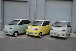 3 kleine Fahrzeuge von Ari Motors in gelb, grün und grau vor einem Gebäude.