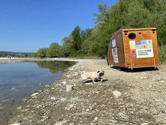 Fahrradanhänger für die EU Ecolabel Roadshow, aus Holz, an einem Ufer am See. Ein Hund im Vordergrund und Bäume im Hintergrund.