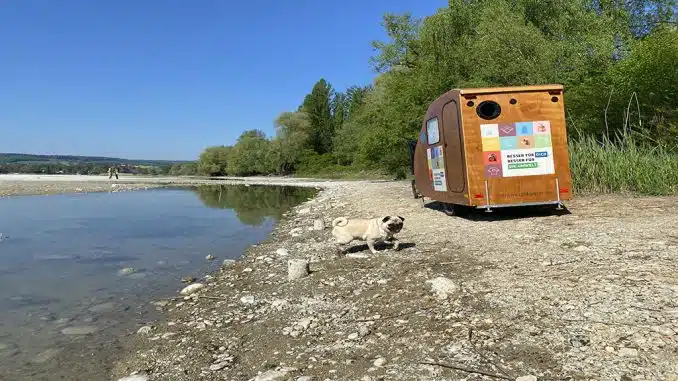 Fahrradanhänger für die EU Ecolabel Roadshow, aus Holz, an einem Ufer am See. Ein Hund im Vordergrund und Bäume im Hintergrund.