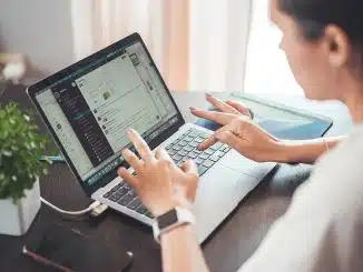 Frau tippt auf einem Laptop an einem Holztisch.