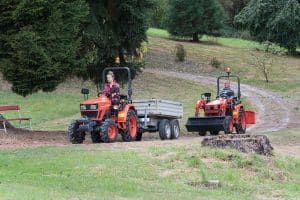 Kubota Modell EK1261 als Frontlader, mit einem Anhänger, fährt einen Hügel herunter. Dahinter ein weiteres Kubota Modell.