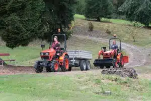 Kubota Modell EK1261 als Frontlader, mit einem Anhänger, fährt einen Hügel herunter. Dahinter ein weiteres Kubota Modell.