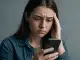 Frau schaut voller Sorge in ihr Handy wegen Cybermobbing.