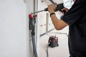 Mann bohrt in die Wand, darunter an der Wand befestigt, befindet sich der Staubsauger von Starmix.