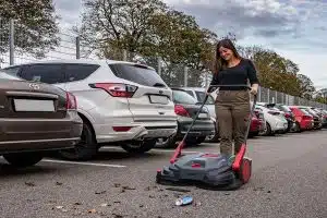 Frau kehrt auf einem Parkplatz mit dem Durosweep Laub vor sich zusammen.