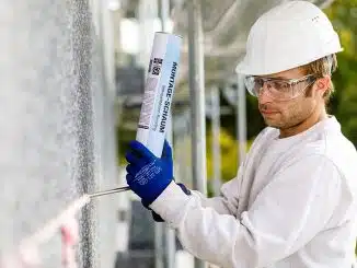 Mann mit Schutzbrille und Helm trägt PU-Schaum an Außenwand auf.