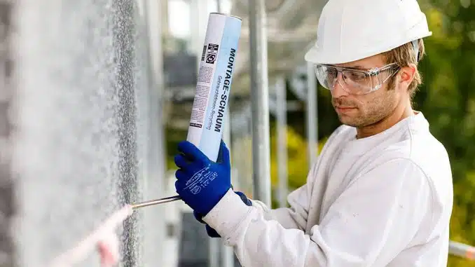 Mann mit Schutzbrille und Helm trägt PU-Schaum an Außenwand auf.