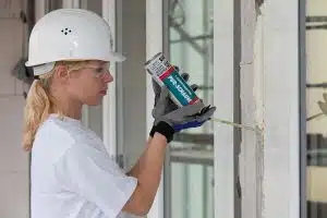 Frau mit Helm und Schutzbrille bringt PU-Schaum zwischen Wand und Fenster an.
